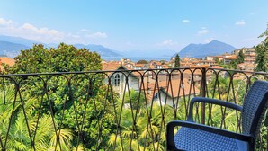 A balcony with a view of a town, a chair, and lush greenery. - Hotel du Parc (Stresa)