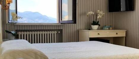 Une chambre d’hôtel avec un lit, un bureau avec un téléphone, un miroir, un radiateur, une télévision et une fenêtre donnant sur un paysage.