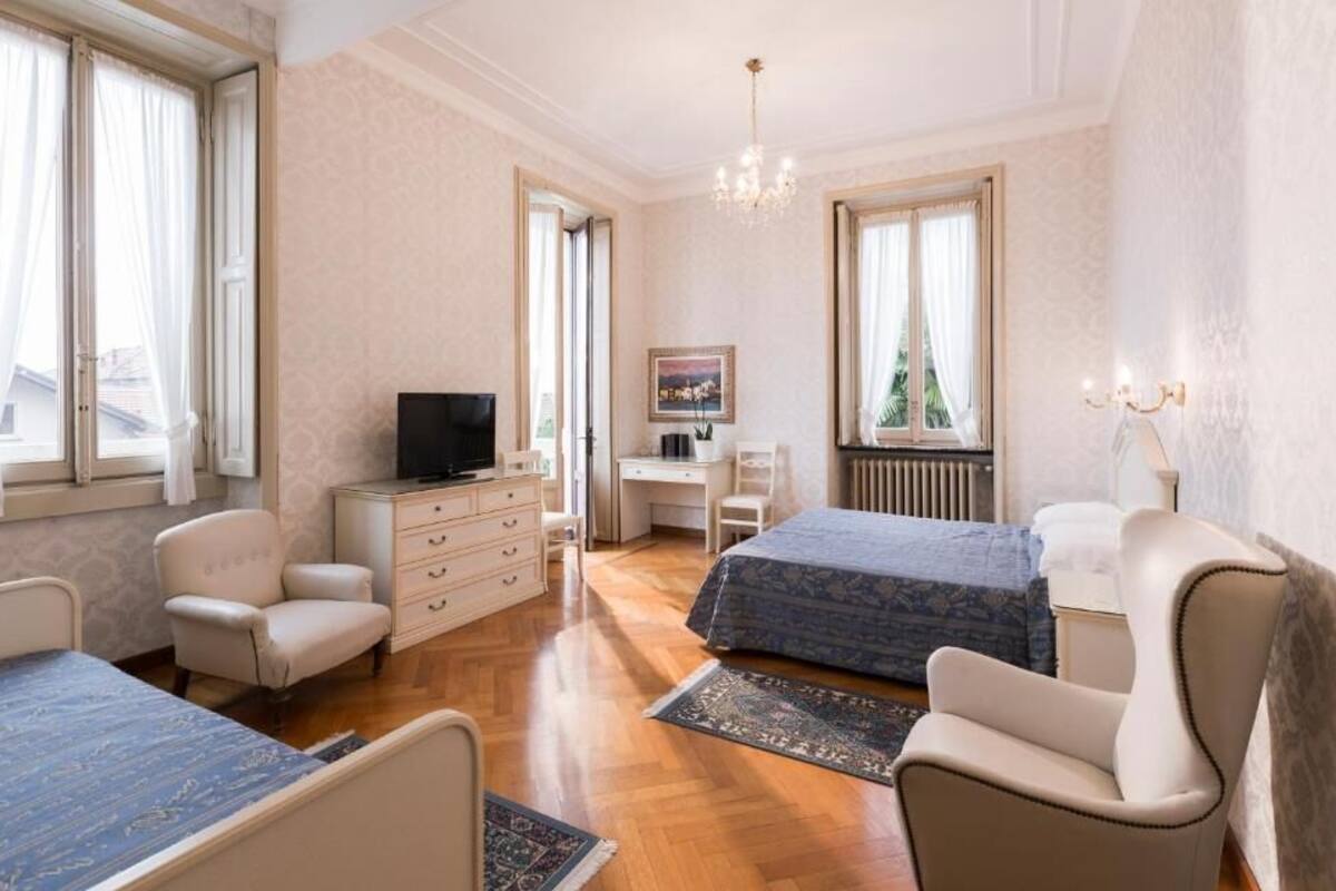 A hotel room with a bed, two chairs, a desk, a television, and a window with curtains.
