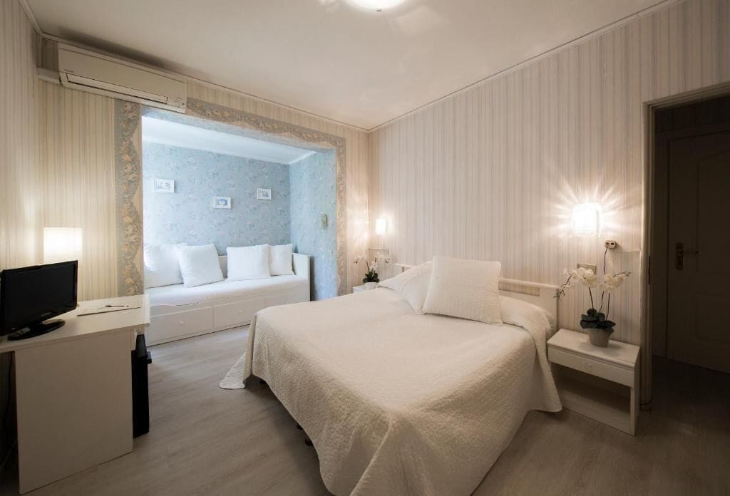 A hotel room with a bed, a desk with a computer, a TV, and a bathroom visible through a door.