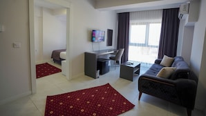 A modern living room with a sofa, a TV, a desk, and a chair. - ELEA PREMİUM STAY Zentrale Standard-Doppel-Suite (PAMUKKALE)