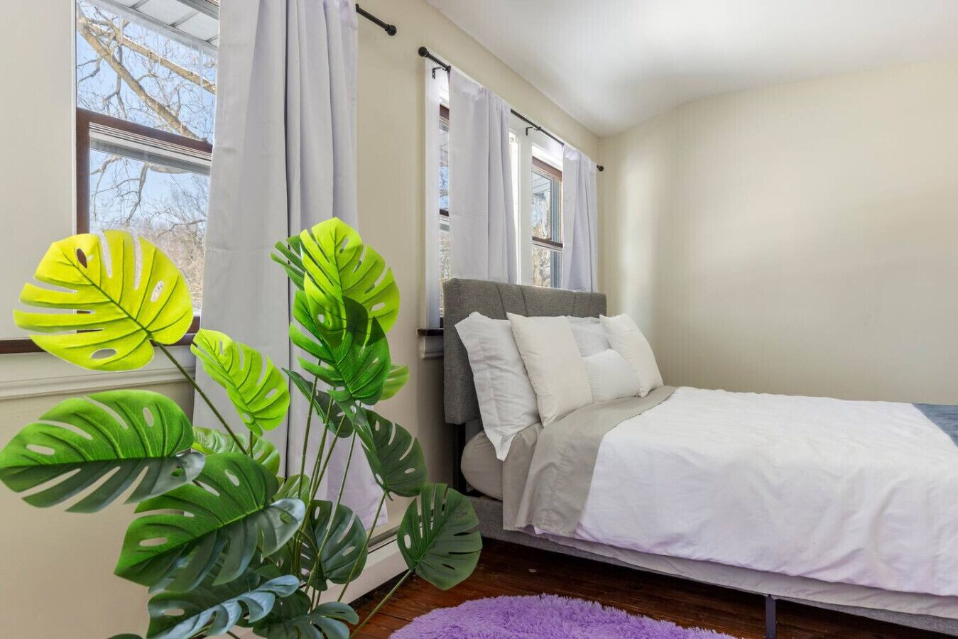 A bedroom with a bed, curtains, a window, and a plant.