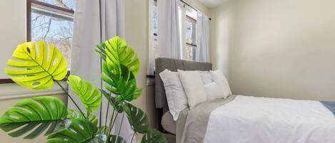 A bedroom with a bed, curtains, a window, and a plant.