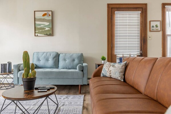 A living room with a light blue sofa, a brown leather sofa, a round wooden coffee table, and a cactus plant. - South Euclid Joy - 5BR Home (South Euclid)