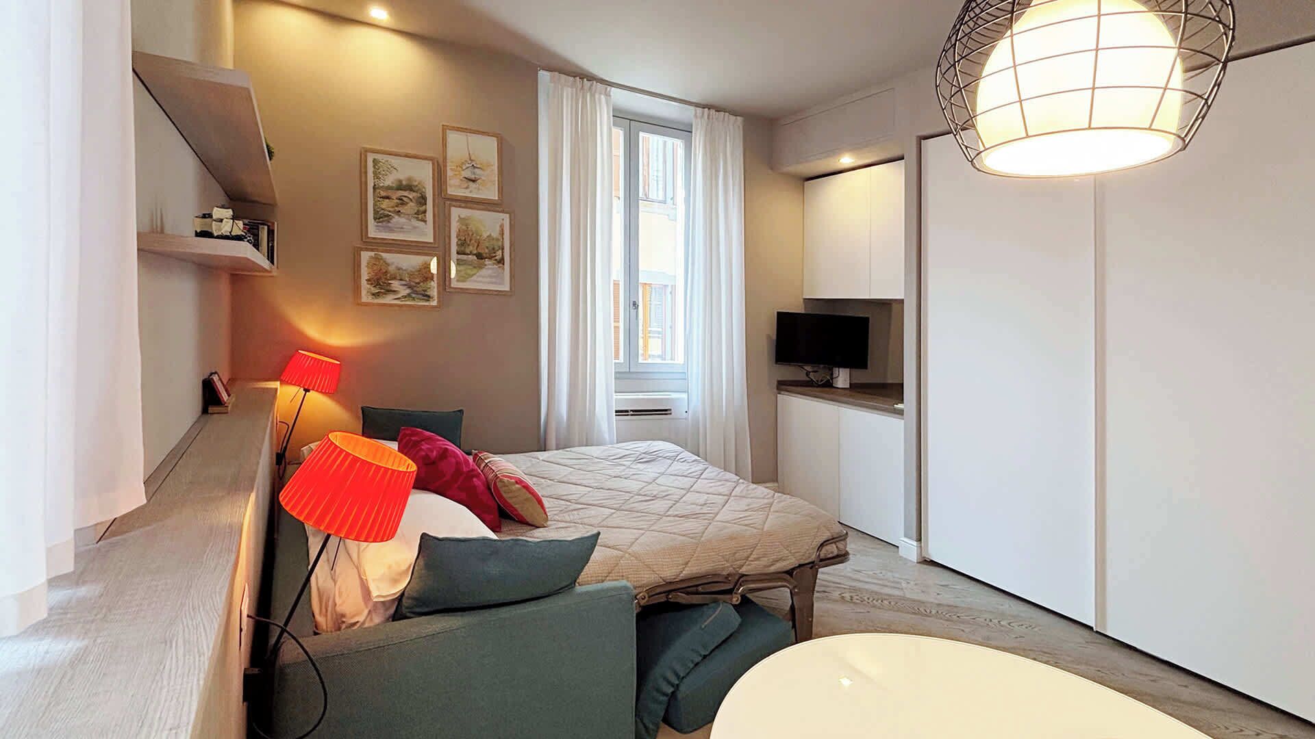 A modern bedroom with a bed, bedside lamps, a TV, and a wardrobe.