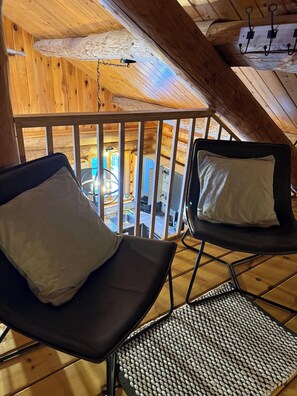 A wooden interior with two reclining chairs, a metal floor, and a view of a kitchen area. - Chalet en bois rond avec spa et foyer, à 10 min du Village Vacances Valcartier (Saint-Gabriel-de-Valcartier)