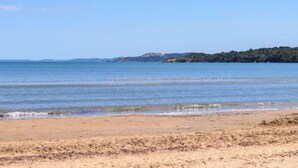 Uma praia com águas claras, areal arenoso e colinas ao longe.