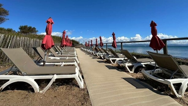 Um calçadão à beira-mar com fileiras de espreguiçadeiras e guarda-sóis vermelhos, que se estende até o mar.