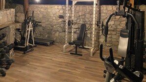 Ein Fitnessraum mit unterschiedlicher Trainingsausstattung, einer Steinwand und einem Holzboden.