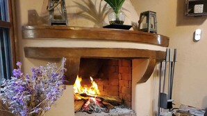 Ein Wohnzimmer mit Kamin, einem Blumentopf, einer Vase mit Blumen und einem Holztisch.