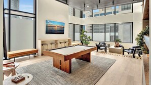 Un espace intérieur moderne doté d’une table de billard, d’un coin salon et de grandes fenêtres offrant une vue sur la ville.