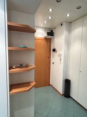 A hallway with a wooden door, a trash bin, and built-in shelves with items on them. - Casa Mira - One Bedroom Apartment, Sleeps 4 (Arenzano)