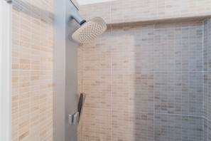 A shower with a handheld showerhead, tiled walls, and a corner showerhead.