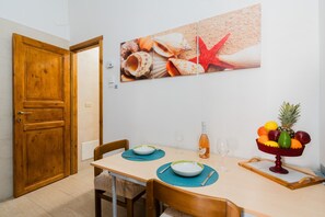 Un comedor con una mesa de madera, sillas, un frutero y un cuadro en la pared con caracoles.