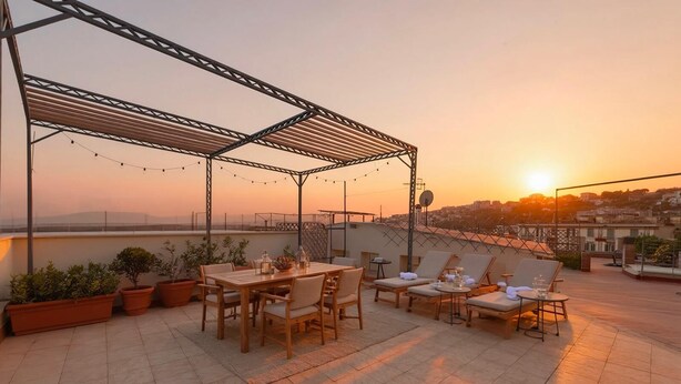 A rooftop terrace with a table and chairs, potted plants, and a view of the sunset over a cityscape. - Luxury Apartment for 5 with Terrace in Chiaia (Napoli)