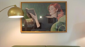 A framed painting of a woman reading a book, a green couch, and a gold lamp on a wall. - Luxury Apartment for 5 with Terrace in Chiaia (Napoli)