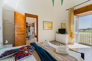 A bedroom with a bed, a TV, a bathroom, and a balcony with a view.