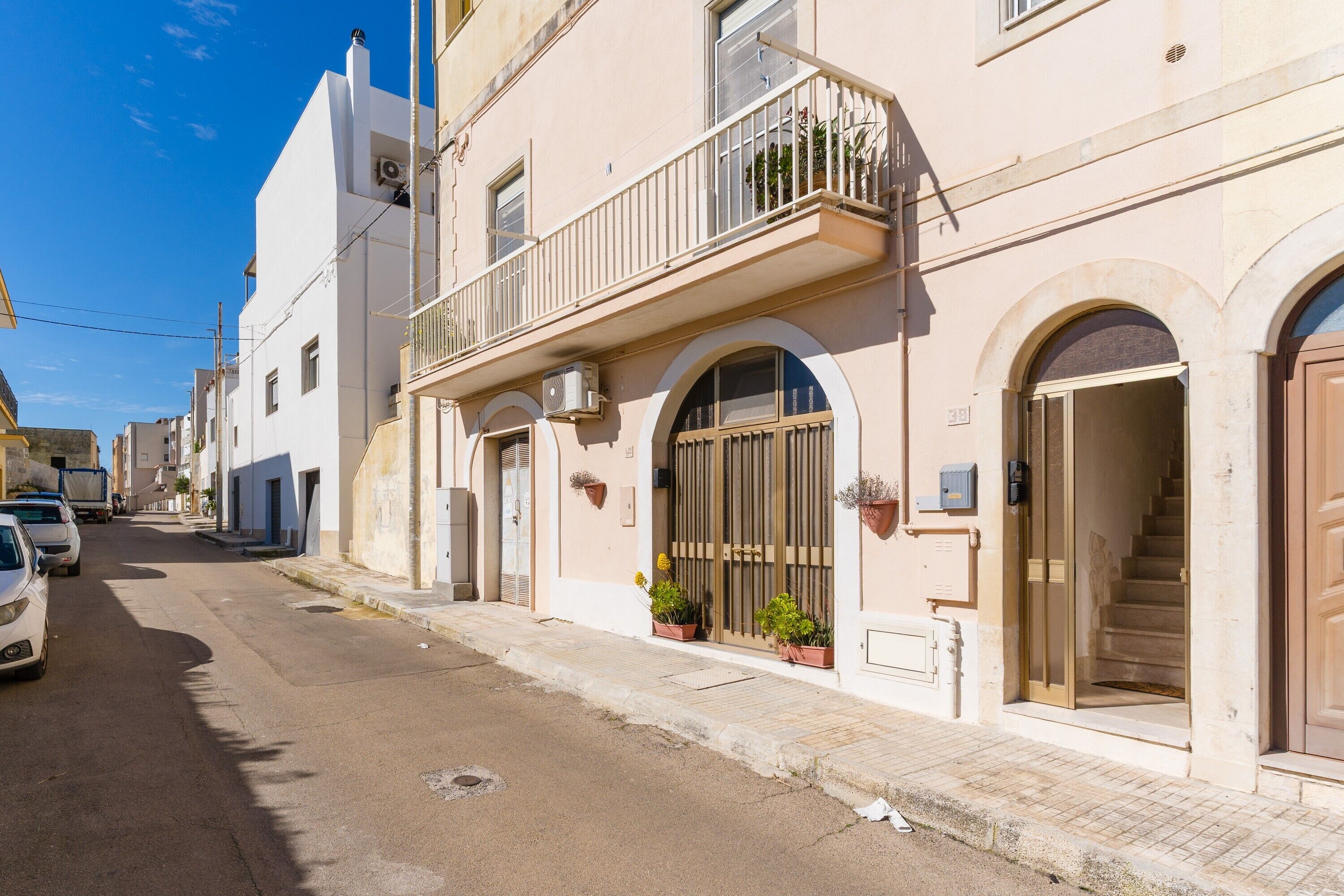 A street view of a building with a balcony, arched windows, and a staircase leading to the entrance.