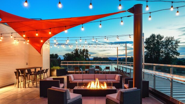 An outdoor patio with a fire pit, seating, and string lights.