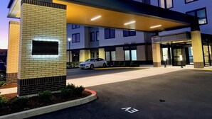 A modern hotel entrance with a covered walkway, a car parked in the lot, and a clear sky.