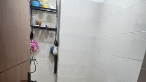 Et lille badeværelse med toilet, håndvask, bruser og en hylde med toiletartikler.
