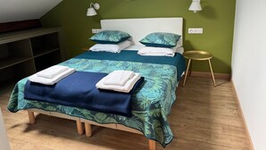 A neatly made bed with a leaf-patterned bedspread, two bedside lamps, a small round table, and a framed picture on the wall.