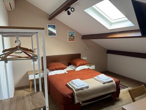 A bedroom with a bed, a desk, a chair, a wardrobe, a skylight, and two wall-mounted pictures.