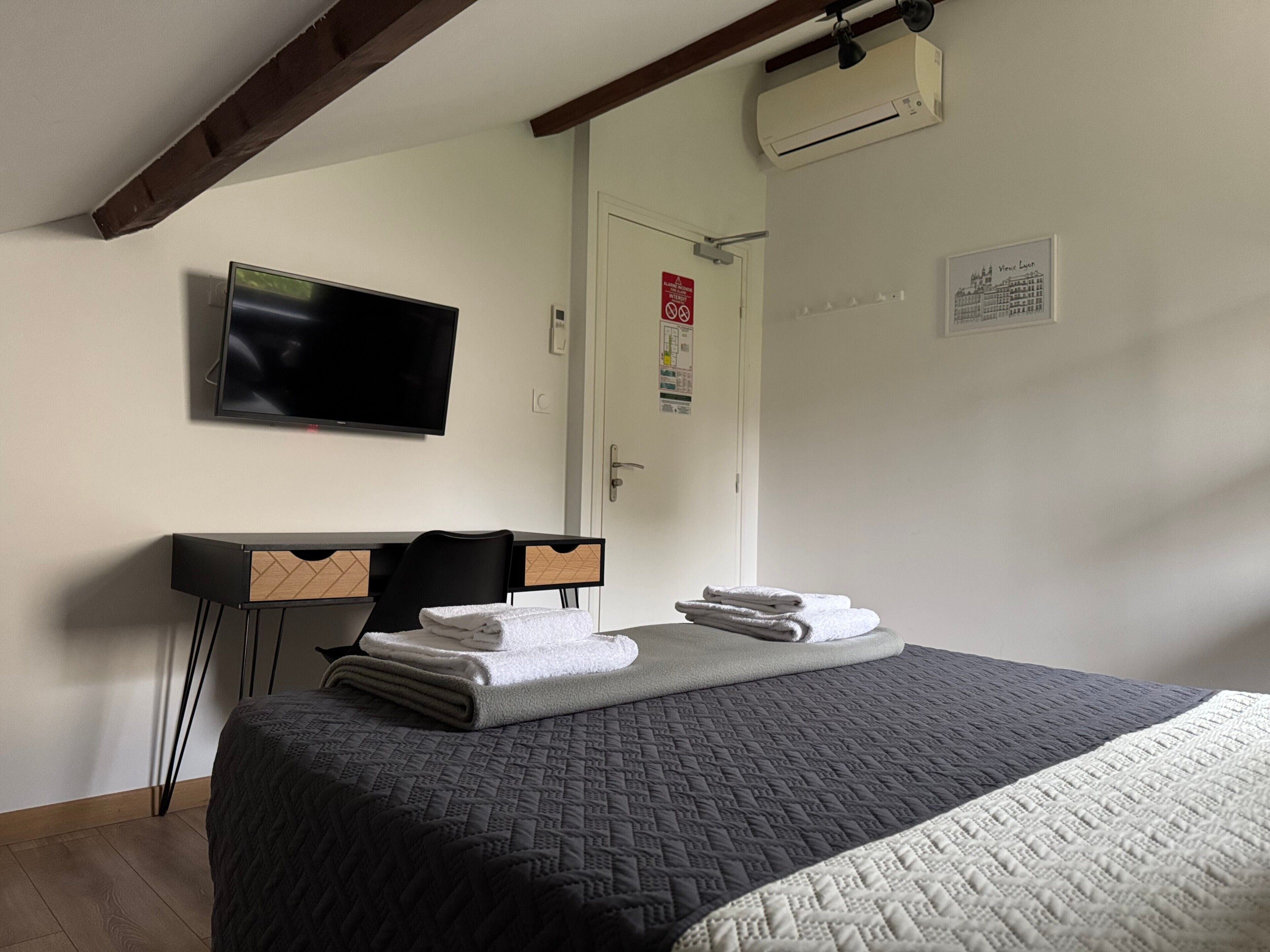 Habitación de hotel con cama, escritorio, silla, televisor de pantalla plana, equipo de aire acondicionado y puerta con letrero de seguridad.