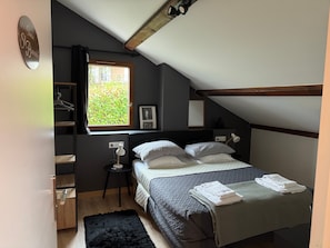 Un dormitorio con cama, mesita de noche, lámpara, ventana con vistas a zonas verdes y una puerta con un letrero.