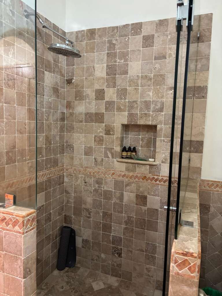 A shower with a glass door, tiled walls, and a shelf with toiletries.