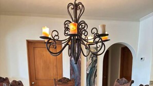 A dining table with six chairs, a chandelier, and a wooden door in the background. - Beautifully Maintained 2-bed Condo in Las Mañanitas (San José del Cabo)