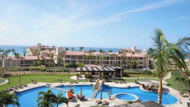 A resort with a large swimming pool, multiple buildings, and palm trees. - Beautifully Maintained 2-bed Condo in Las Mañanitas (San José del Cabo)