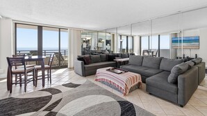 Ein großzügiger Wohnbereich mit einer großen Couch, Esstisch und Stühlen, einem Balkon mit Blick und einer modernen Küche im Hintergrund.