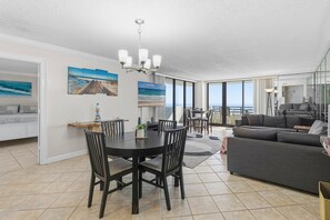 A spacious living area with a dining table, a sofa, and large windows offering a view. - Horizons 1502 (Daytona Beach)