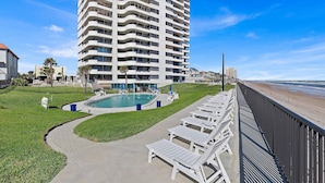 Ein Hochhaus-Hotel mit Swimmingpool, Liegestühlen und Blick auf den Strand.