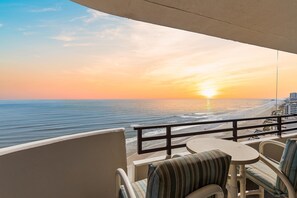 A balcony with a view of the ocean at sunset, a table, and two chairs. - Horizons 1502 (Daytona Beach)