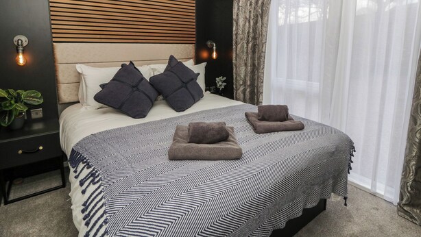 Un dormitorio moderno con una cama grande, dos lámparas de noche, un cabecero con diseño de listones de madera y cortinas translúcidas en la ventana.