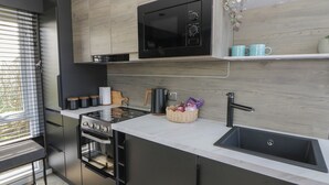 Una cocina moderna con microondas integrado, estufa y pileta. Hay una ventana con persianas, una cesta con botanas y una taza de café en la encimera.