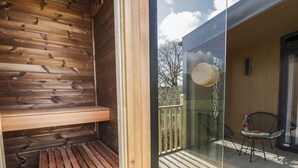 Un sauna de madera con bancos y una puerta de vidrio que da a una terraza exterior con sillas y una mesa.