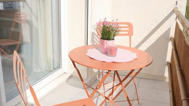 Ein Balkon mit Tisch und Stühlen, einem Blumentopf und Blick durch eine Glastür.