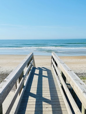 Un paseo marítimo de madera que conduce a una playa con vistas al océano.