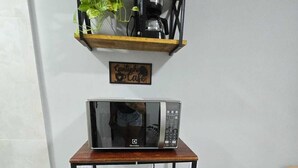 A compact kitchenette with a microwave, a small refrigerator, a coffee maker, and a potted plant on a shelf. - Alex Sandro (Rio das Ostras)