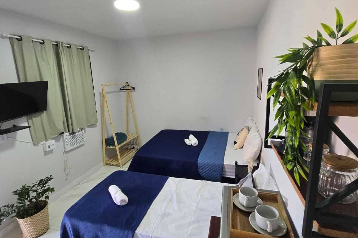Una habitació d'hotel amb dos llits, una televisió, una taula de treball i una cafetera, a més d'una planta.