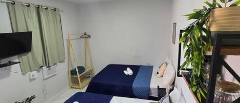 A hotel room with two beds, a TV, a desk with a coffee maker, and a plant.