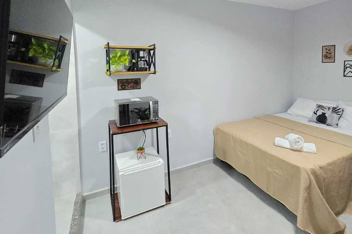 Una habitació petita i moderna amb un llit, una taula amb microones, una televisió penjada a la paret i una làmpada al sostre.