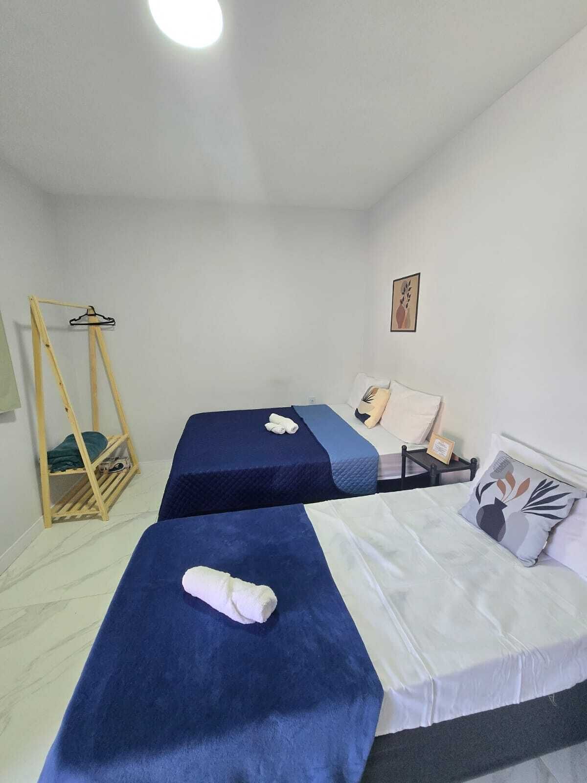A room with two beds, a wooden swing chair, a small table, and a picture on the wall.
