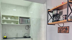 A compact kitchen with white cabinets, a microwave, a coffee machine, and a sign reading 'Cantinho Cafe'. - Alex Sandro (Rio das Ostras)