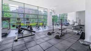 Et fitnesscenter med forskellig træningsudstyr, store vinduer og udsigt til bygninger og træer.