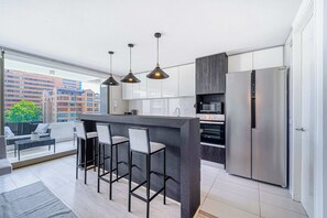A modern kitchen with a central island, bar stools, stainless steel appliances, and a view of the city. - Nordic Home - 2BR, Parking, Wifi & Shopping Mall (Santiago)