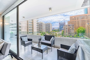 A balcony with wicker furniture, a glass table, and a city view. - Nordic Home - 2BR, Parking, Wifi & Shopping Mall (Santiago)